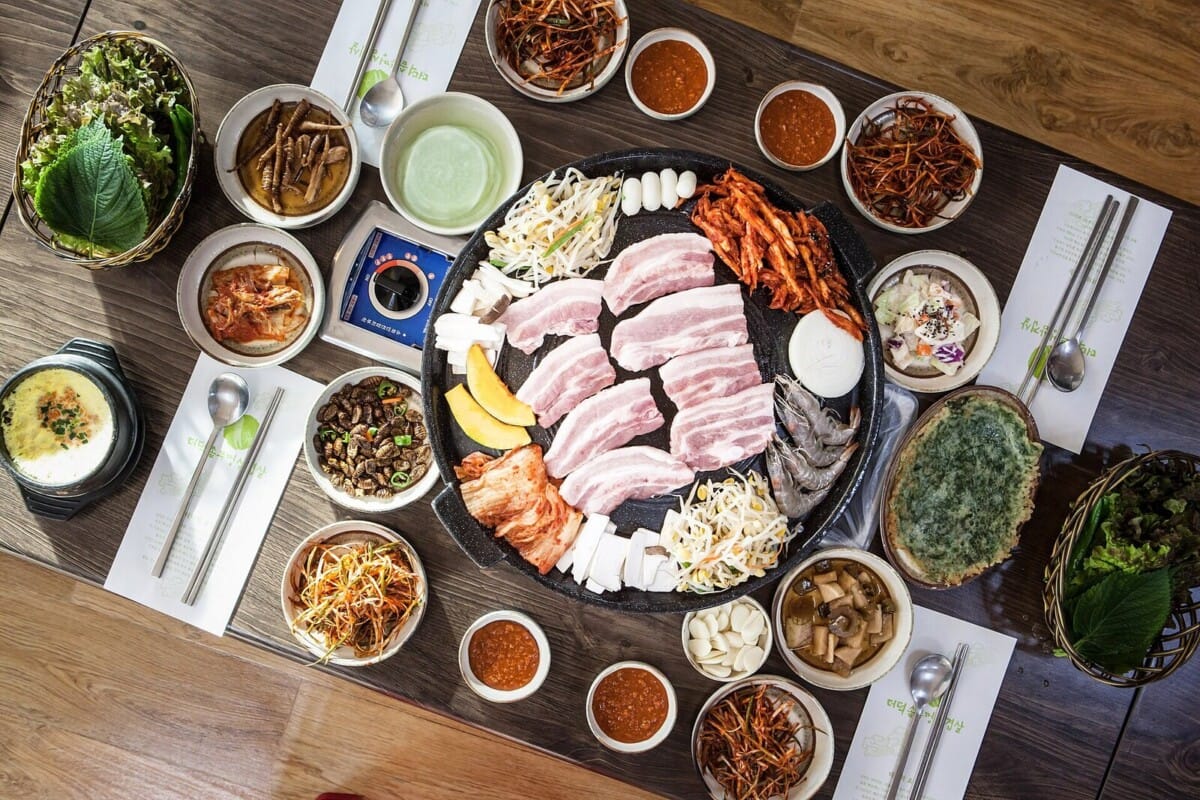 솥뚜껑 불판에 올린 삼겹살과 여러 가지 밑반찬이 차려진 한국 고기집 한 상